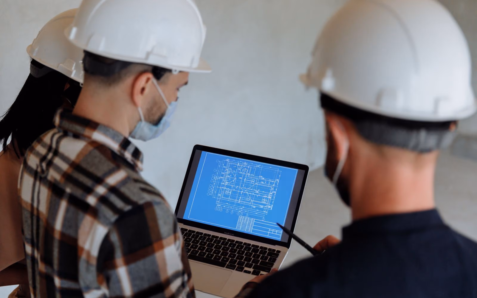 Site team reviewing a blueprint on a laptop, wearing hard hats